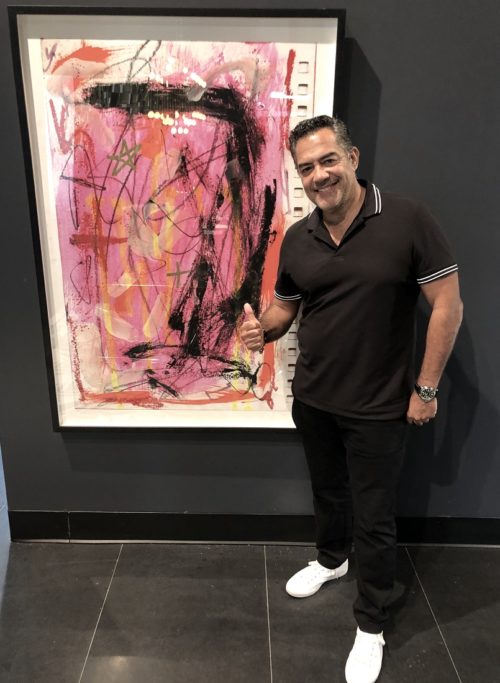 Carlos Gomez next to the painting of artist/actor Yul Vazquez at Galerie D' Oro in the Miami Design District.