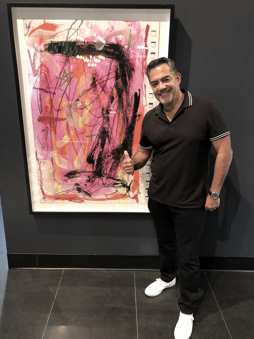 Carlos Gomez next to the painting of artist/actor Yul Vazquez at Galerie D' Oro in the Miami Design District.