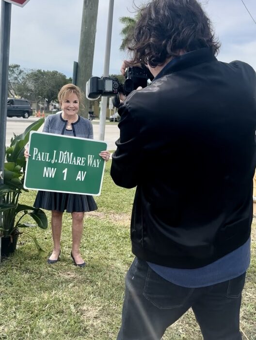 SocialMiami photographer Manny Hernandez captures philanthropist Swanee DiMare holding the sign of the street named for her late husband