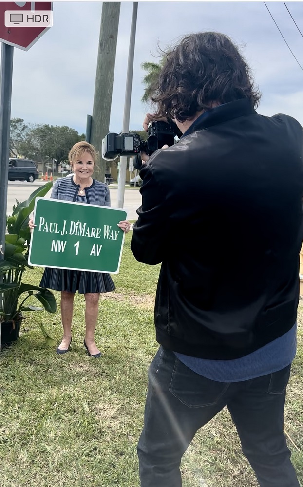 SocialMiami photographer Manny Hernandez captures philanthropist Swanee DiMare holding the sign of the street named for her late husband